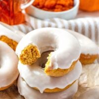 Stacked maple glazed pumpkin donut with a bite taken out of it.