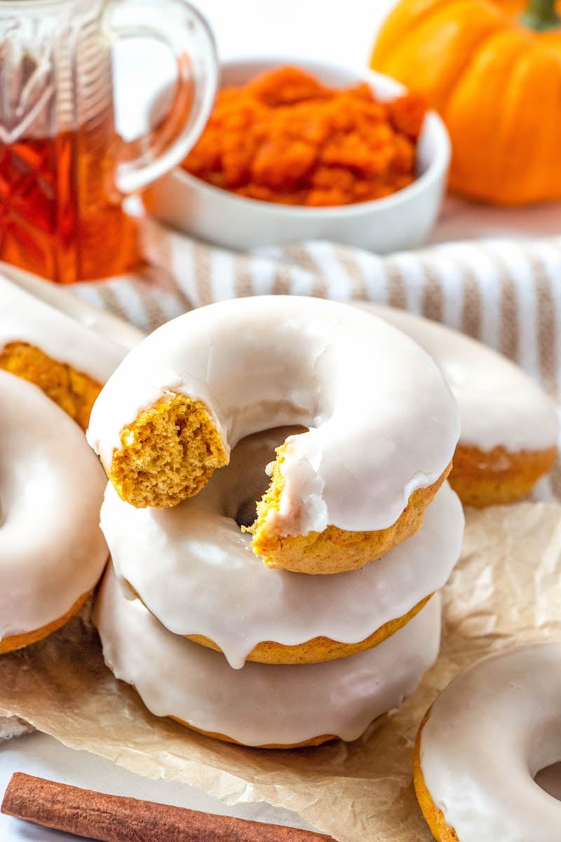 Stacked maple glazed pumpkin donut with a bite taken out of it.