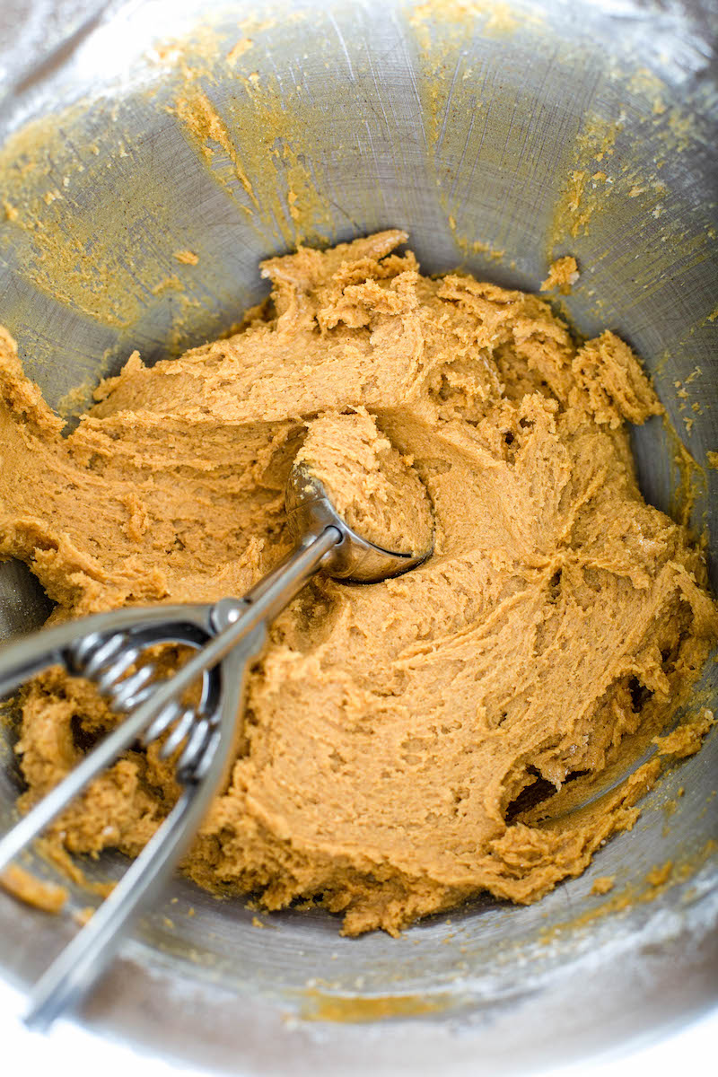 Molasses cookie batter with a cookie scoop in it.