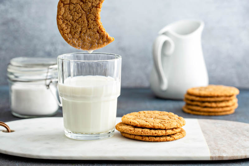 Molasses cookie with a bite taken out of it, over a glass of milk.