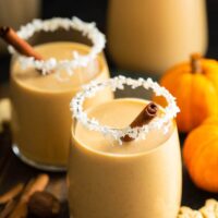 Glasses of pumpkin coquito with cinnamon sticks.
