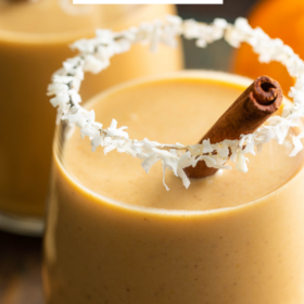 Up close image of Pumpkin Coquito with coconut on the rim of glass and a cinnamon stick inside glass.