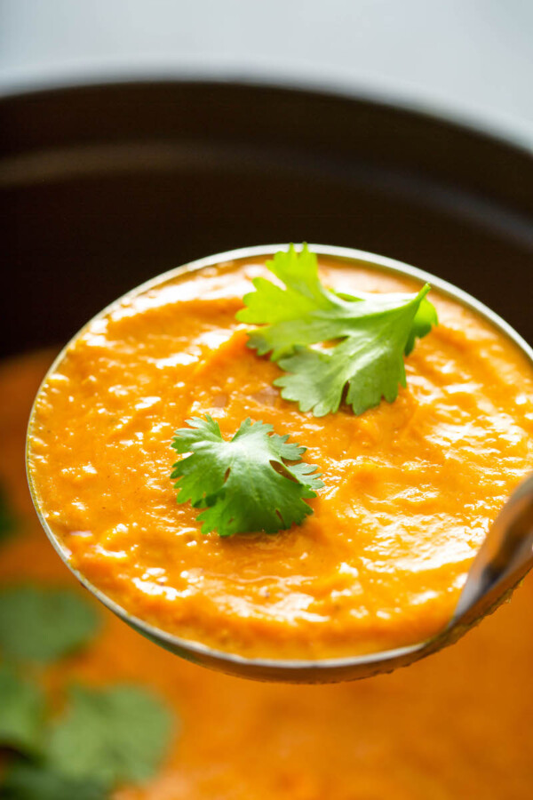 Ladle full of pumpkin soup with cilantro.