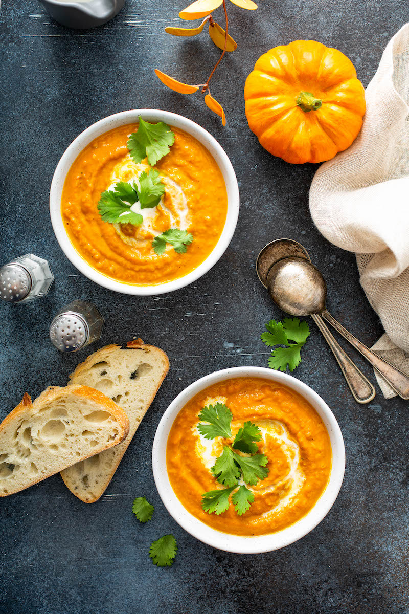 Two bowls of pumpkin soup with bread slices.