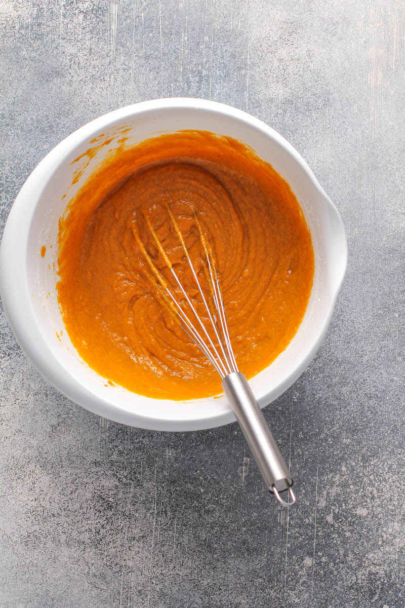 White bowl with pumpkin batter inside with a whisk. 