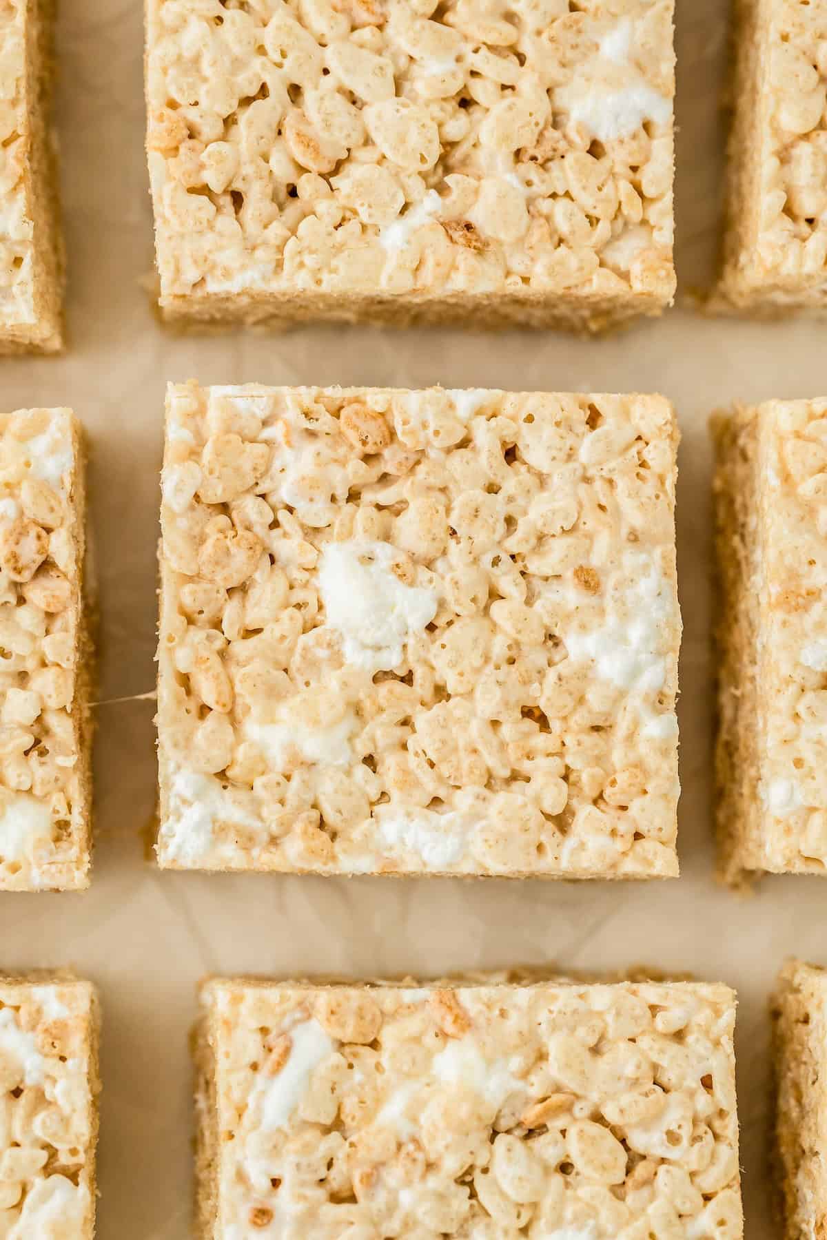 Rice Krispie treats are cut into squares and spread out on a sheet of parchment paper.