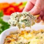 A cracker is lifting a small portion of creamy spinach dip from the baking dish.