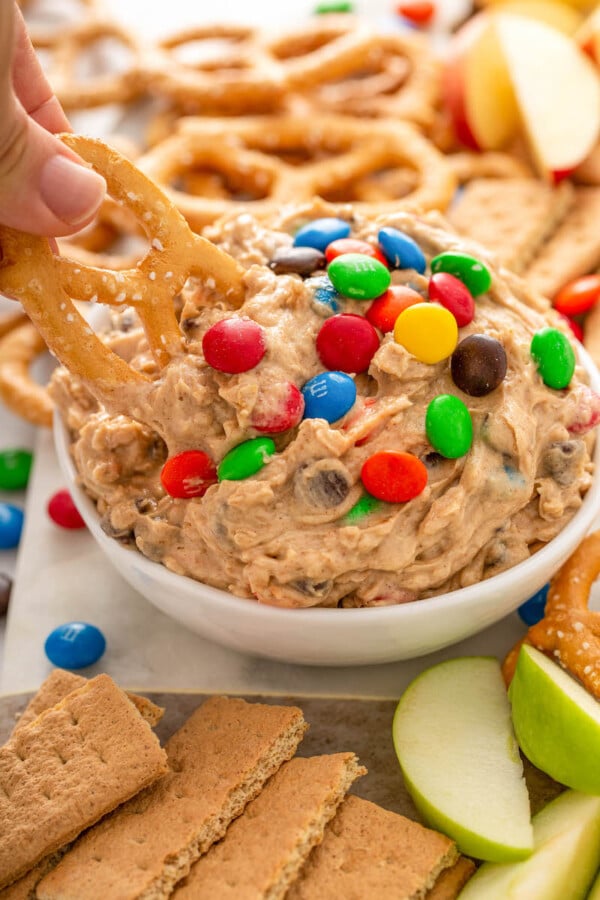 A pretzel is being dipped into a bowl of monster cookie dough dip