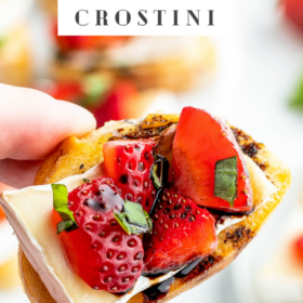 Crostini being held by a hand with strawberries, brie and balsamic vinegar drizzled on top.
