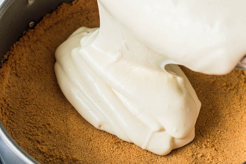 Cheesecake batter being poured onto a graham cracker crust.
