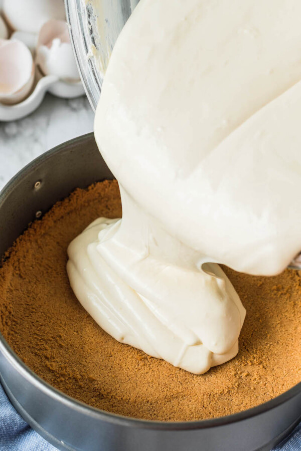 Cheesecake batter being poured onto a graham cracker crust.