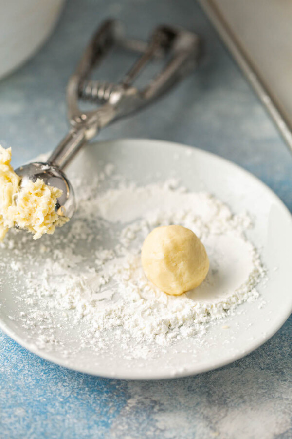 Dough balls are rolled in cornstarch on a white plate.