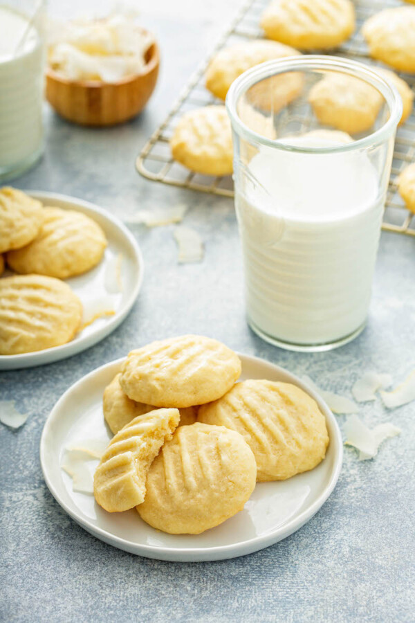 Four cookies are on a white plate next to a full glass of milk.