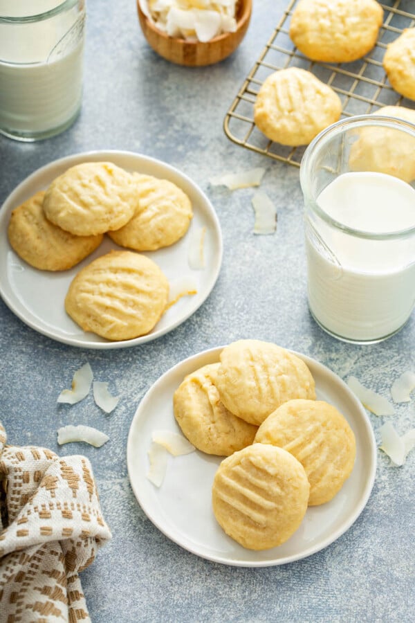 Two white plates have several cookies on top of them with a glass of milk nearby.