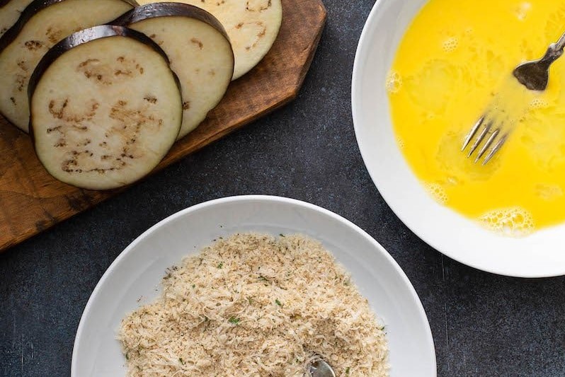 Sliced eggplant, breadcrumbs and egg wash in a bowl