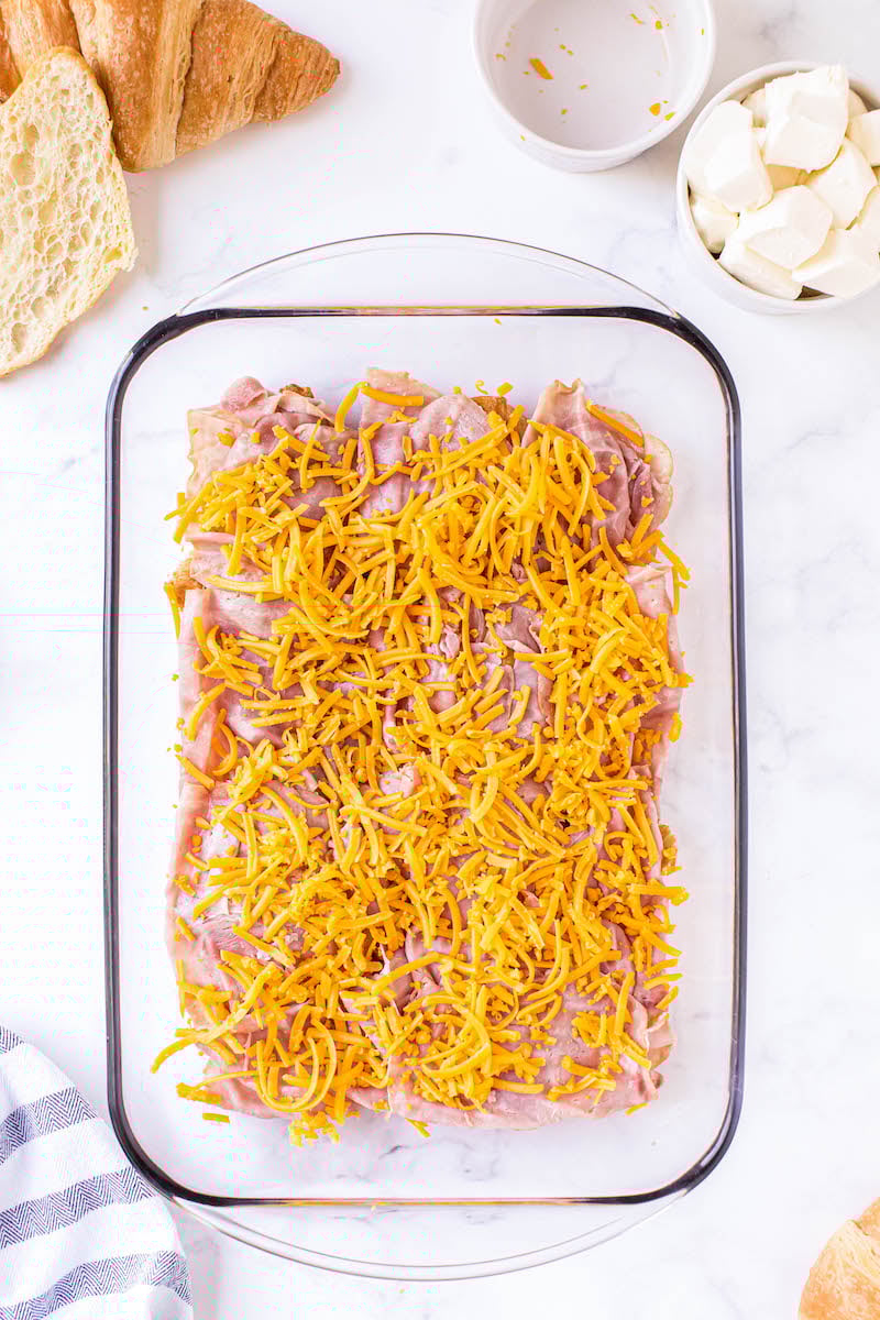 Deli ham topped with shredded cheese in a pan.
