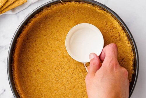 Graham cracker crust being pressed into a springform pan