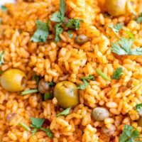 A close up shot of arroz con gandules shoes cilantro, olives, peas and rice.