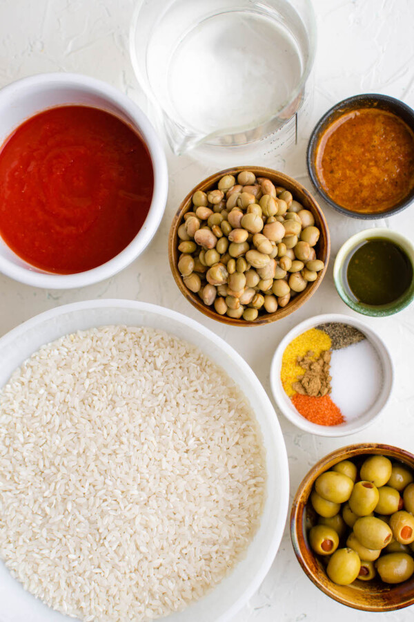 The ingredients for this rice dish are separated in bowls on a white surface.