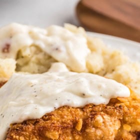 Up close image of chicken fried chicken with gravy on top on a white plate.