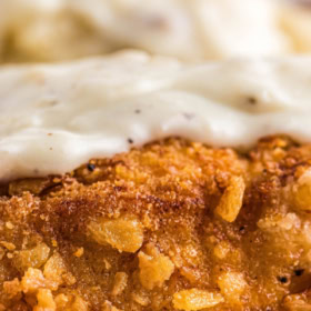 Up close image of chicken fired chicken with gravy on top and mashed potatoes in background.