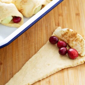 A triangle of crescent roll dough with a slice of cinnamon-coated apple and a few cranberries