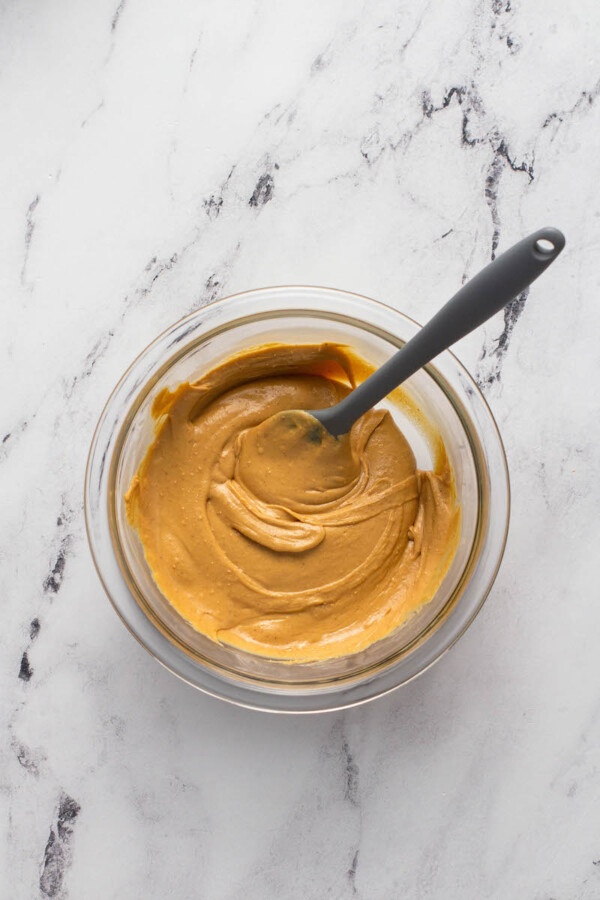 Peanut butter is stirred with a gray spatula in a glass bowl.