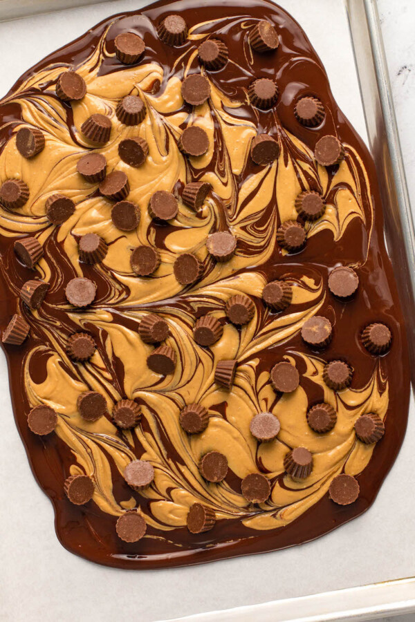 Chocolate peanut butter bark is spread on a prepared baking sheet, ready to be cooled.