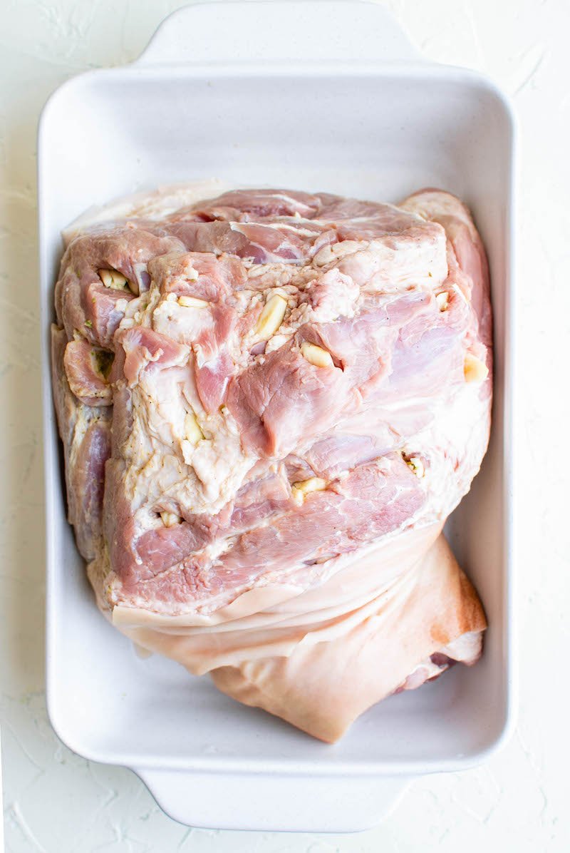 A raw cut of pork meat sits in a white baking dish.