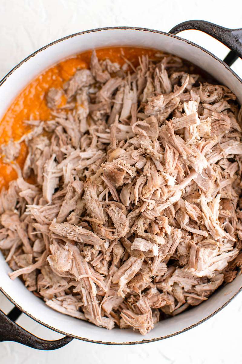 Shredded pork being added to the red sauce.
