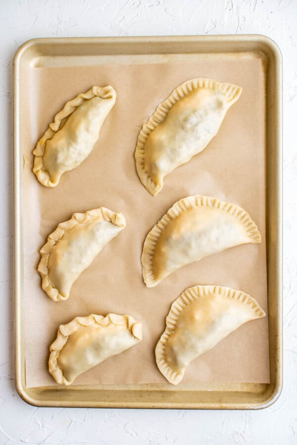 Uncooked empanadas on a tray.