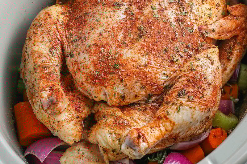 Whole chicken sat inside a crockpot with vegetables under it.