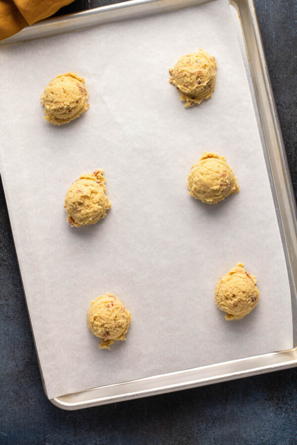 Cookie dough balls are spread out on a prepared baking sheet.