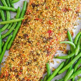 Uncooked Sun-Dried Tomato and Parmesan Crusted Salmon with green beans scattered around on a baking sheet