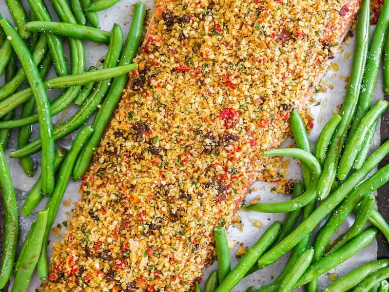 Uncooked Sun-Dried Tomato and Parmesan Crusted Salmon with green beans scattered around on a baking sheet