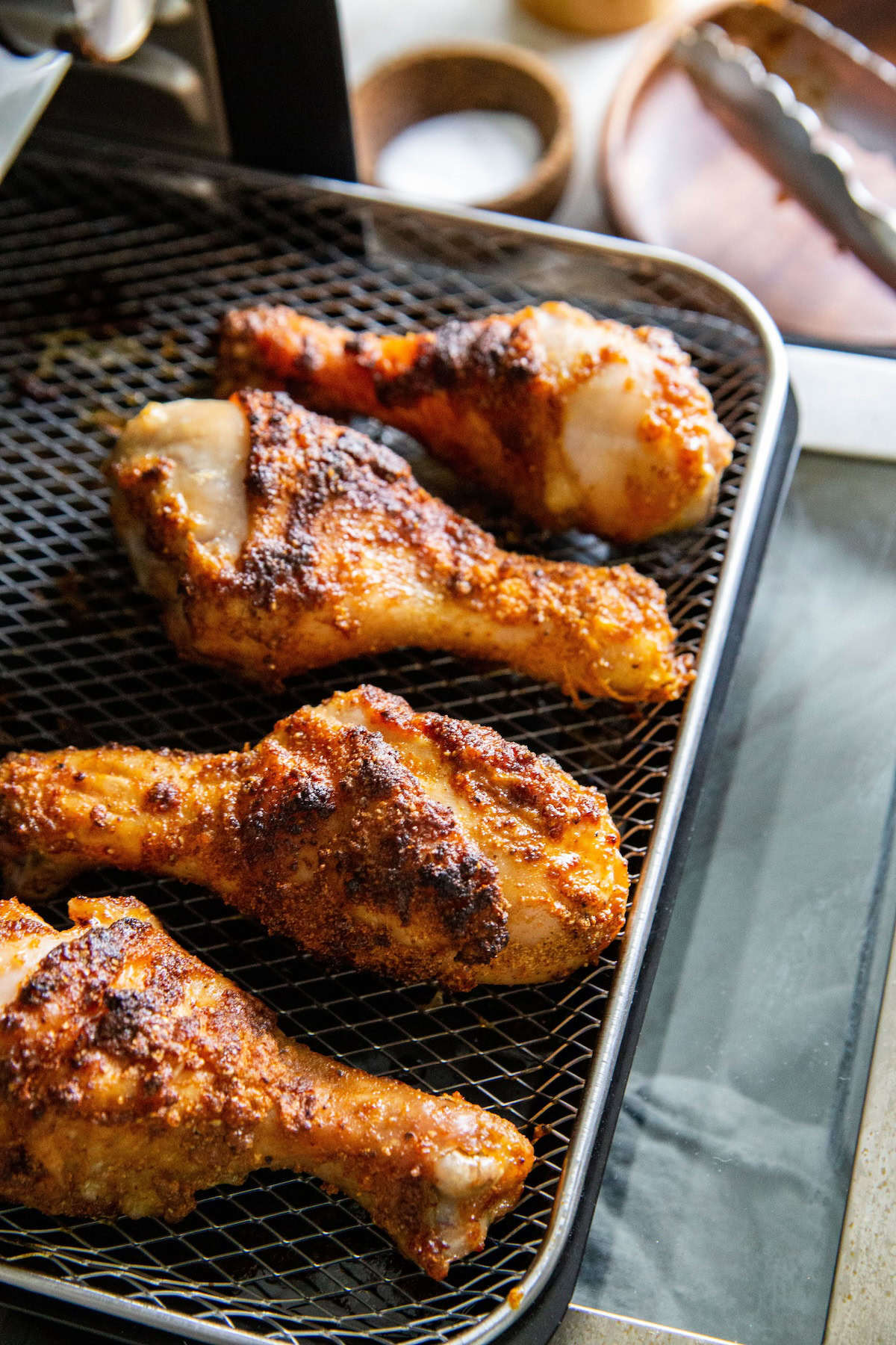 Crispy chicken legs in air fryer set on the metal wire basket.