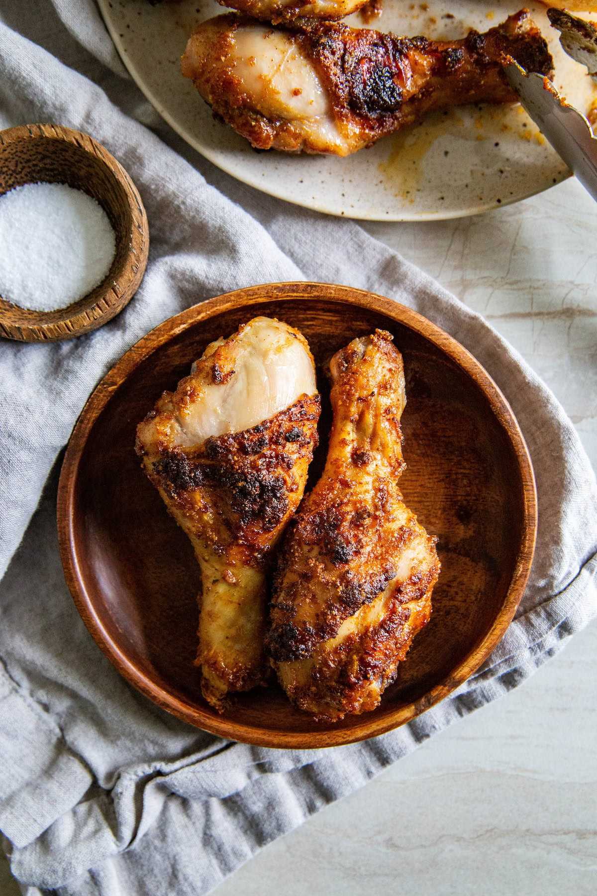 A couple of crispy brown sugar chicken legs are placed in a small wooden bowl. 