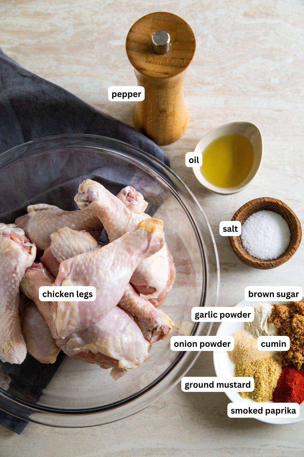 Ingredients for brown sugar air fryer chicken legs recipe arranged in bowls. From top to bottom: pepper, oil, chicken legs, salt, brown sugar, garlic powder, onion powder, cumin, ground mustard and smoked paprika. 