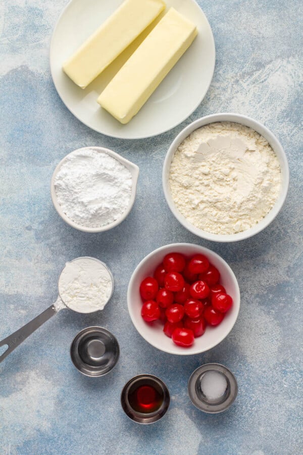 Ingredients for shortbread cookies in white jars on a blue background.