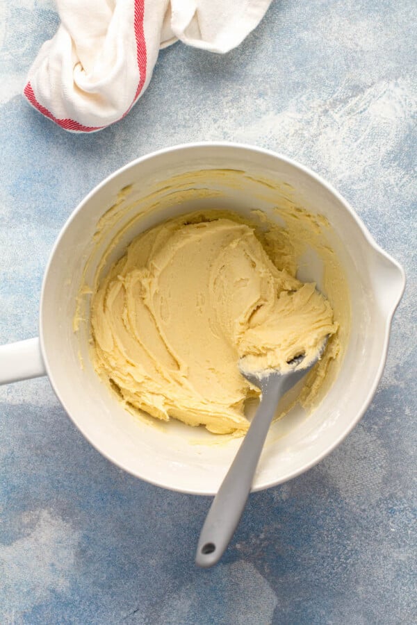 White bowl with cookie dough in it with a spatula and towel.