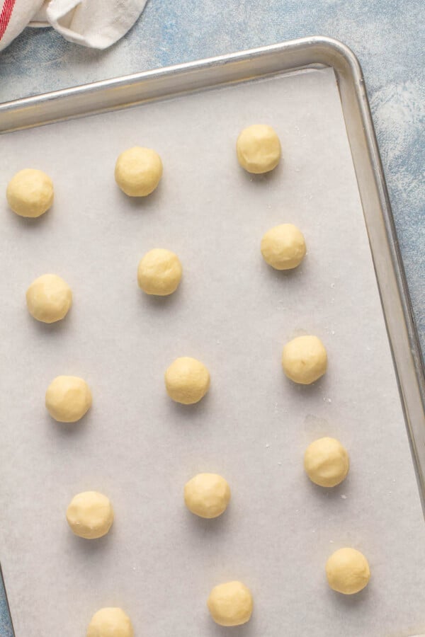 Whipped shortbread cookie dough rolled into palls and placed on a cookie sheet with parchment paper.
