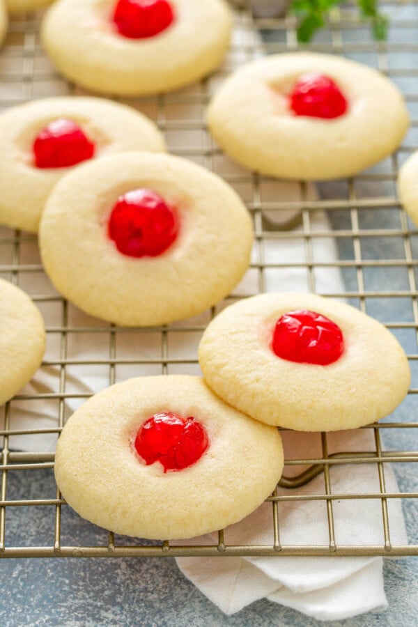 Almond shortbread cookies with a cherry in the center on a cooling rack.