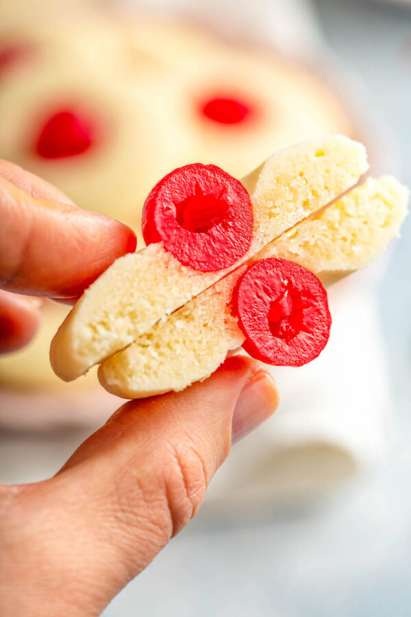Shortbread cookie with a cherry in the center cut in half being held in between two fingers.