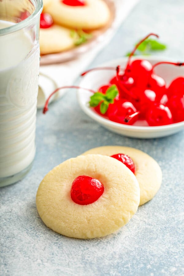 Two cookies stacked on top of each other with cherries and milk in a glass in the background.