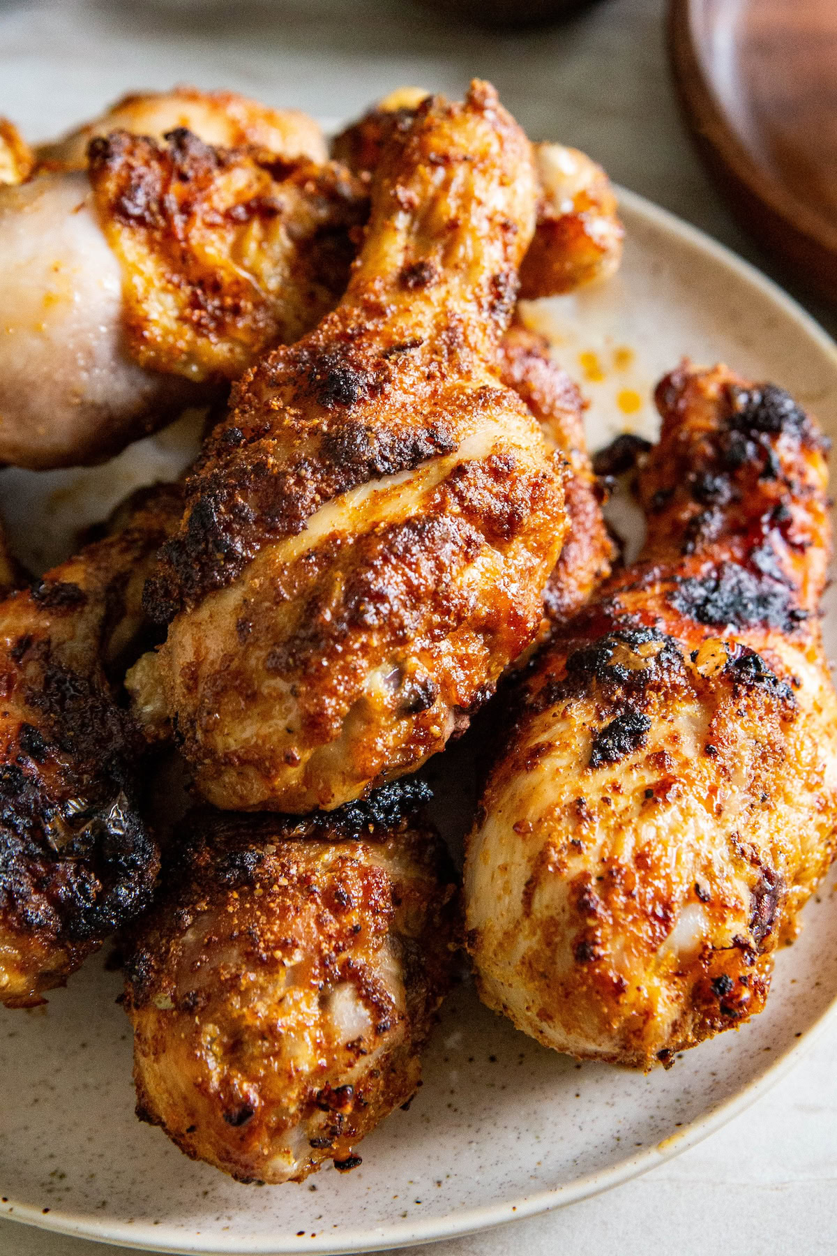 A pile of sweet and savory brown sugar chicken legs cooked in the air fryer are placed on a white plate. 