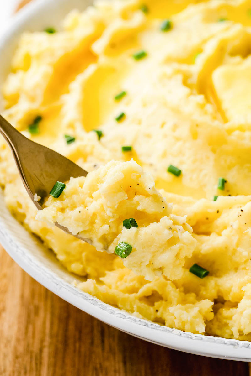Wooden spoon in a plate of garlic mashed potatoes.
