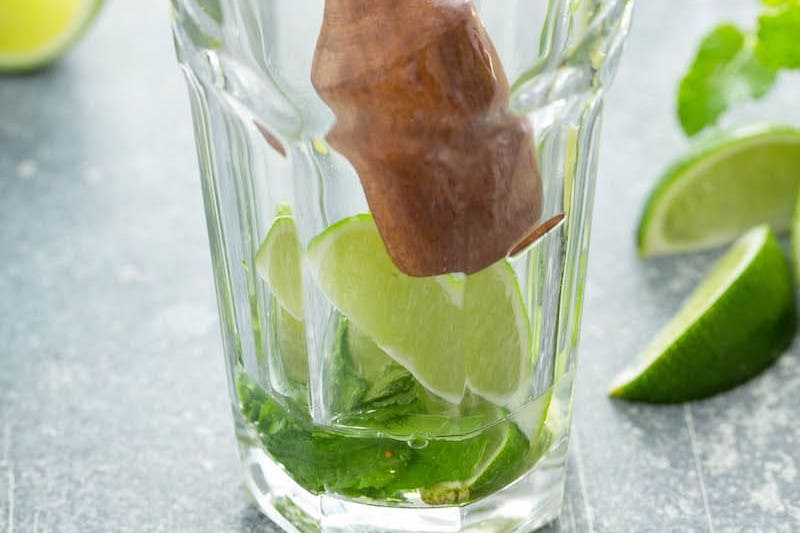 Mint and lime wedge at the bottom of a glass with a muddler on top.