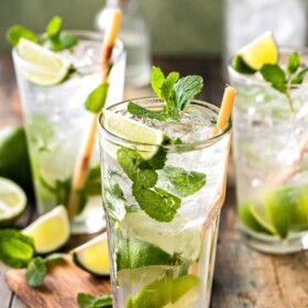 3 mojitos with mint leaves and lime wedges.