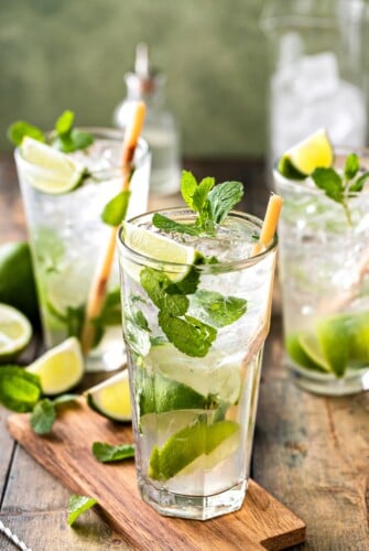 3 mojitos with mint leaves and lime wedges.