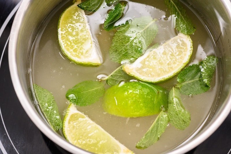 Lime wedges and mint floating in a simple syrup in a sauce pan.